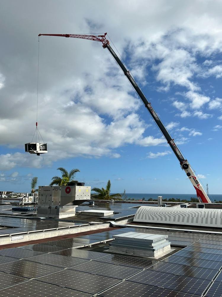Grue mobile avec fléchette posant un équipement sur une toiture photovoltaïque
